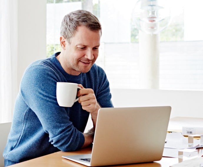 男子在家中边喝咖啡边使用笔记本电脑。